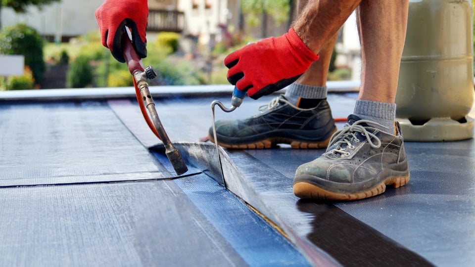 Roofers installing ice barrier self-adhering underlayment at roof eaves to meet Kentucky building code requirements for cold climate protection
