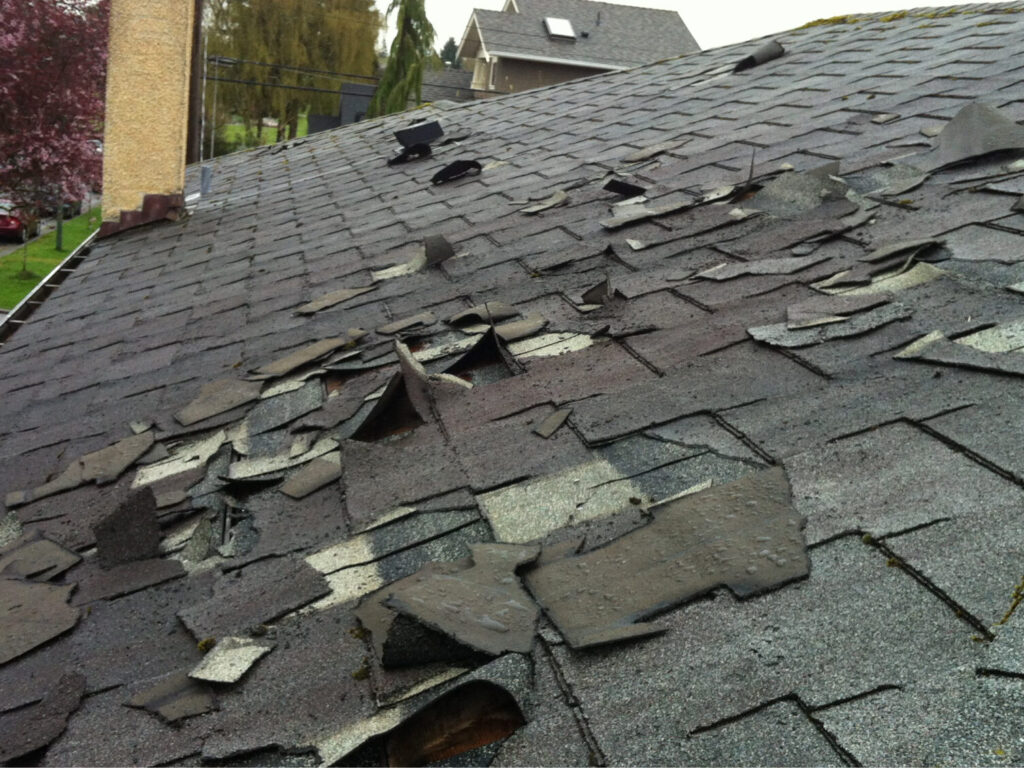 A damaged asphalt shingle roof with visible storm damage