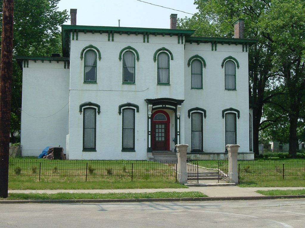 1863 Italianate mansion in Portland, Louisville, Kentucky, with a white stucco facade, green cornice trim, arched windows, and a wrought iron fence
