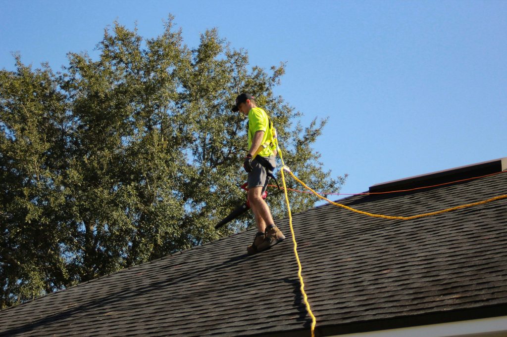 Roofing worker installing solar equipment on a rooftop while secured with a safety rope